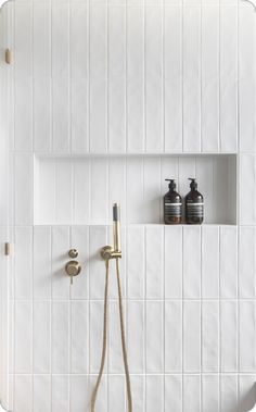 a white tiled bathroom with two soap dispensers on the wall and a shower head