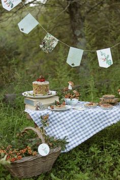 a picnic table is set up in the woods with cake and tea cups on it