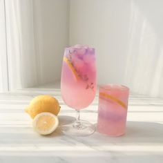 two glasses filled with pink and yellow liquid next to lemons on a white table