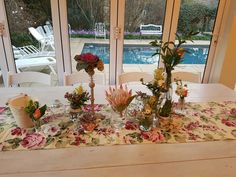 a table with flowers and vases on it in front of a window overlooking a swimming pool