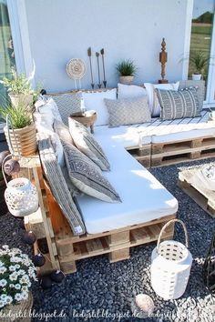 a couch made out of wooden pallets with pillows on it and some plants in the background