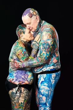 a man and woman covered in tattoos hugging each other with their arms wrapped around each other