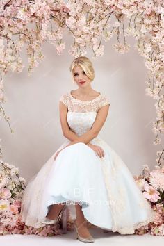 a woman in a white dress is sitting on a bench with pink flowers behind her