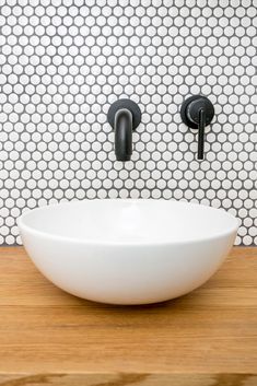 a white bowl sitting on top of a wooden counter next to two black faucets