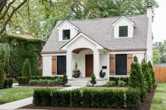 a white house with brown shutters and trimmed hedges around it's front door