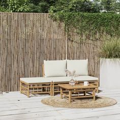 a couch and coffee table on a wooden deck in front of a bamboo privacy wall