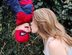 a woman kissing a young boy with spiderman on his face in front of bushes