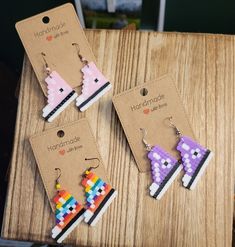 three pairs of handmade earrings are displayed on a wooden table next to each other