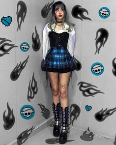 a woman in a kilt and boots standing next to a wall with skulls on it