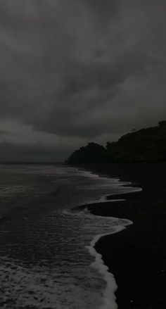 black sand beach with waves coming in to shore and dark cloudy sky above, on an overcast day