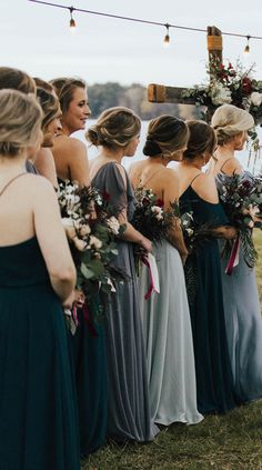 a group of women standing next to each other wearing dresses and holding bouquets in their hands