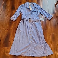 a blue shirt dress is laying on the floor next to a pair of white shoes