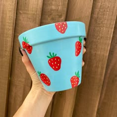 a hand holding a blue cup with strawberries on it