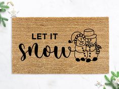 a door mat with the words let it snow on it and a drawing of two people hugging