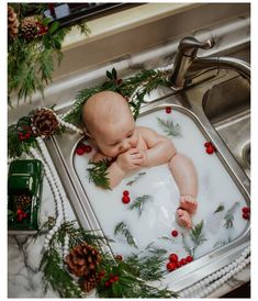 a baby is taking a bath in a sink with christmas greenery on the edge