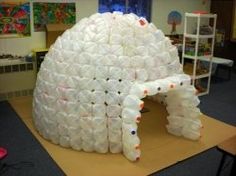 a large white building made out of plastic bottles on top of a wooden table in a room