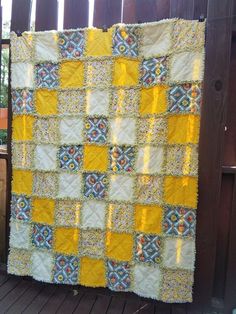 a yellow and blue quilt hanging on a wooden fence