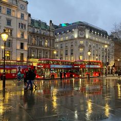 two red double decker buses parked in front of tall buildings on a wet street at night