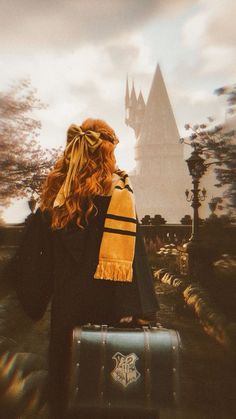 a woman with red hair is carrying a suitcase in front of a hogwarts castle