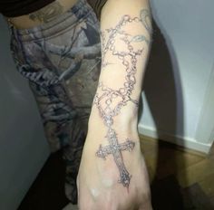 a person with a tattoo on their arm holding a cross and rosary bracelet in front of them