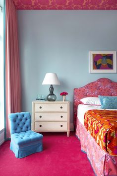 a bedroom with pink carpet, blue walls and a colorful bed in the corner next to a chair