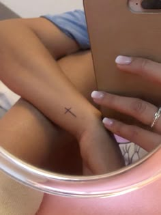 a woman's hand holding a cell phone with a cross tattoo on it