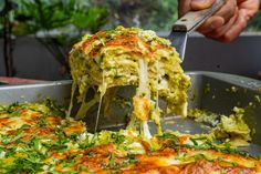 someone is cutting into a pizza with cheese and herbs on it in a metal pan