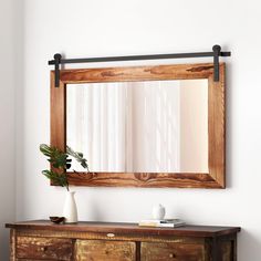 a mirror hanging on the wall above a dresser with a potted plant next to it