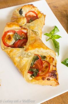 two pieces of pizza on a white plate with basil leaves and tomatoes in the background