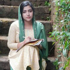 a woman sitting on some steps with a book in her hand and looking at the camera