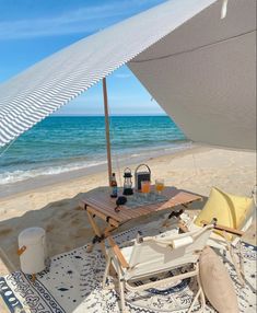 an umbrella and chairs on the beach with drinks in front of it, next to the ocean