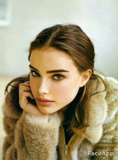 a beautiful young woman wearing a fur coat and holding her hand on her chin, looking at the camera