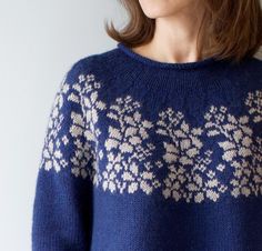 a woman wearing a blue sweater with white flowers on it