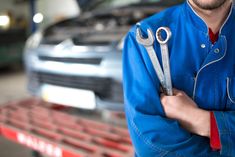 a man holding two wrenches in front of a car