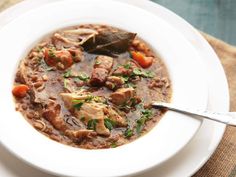 a white bowl filled with meat and vegetable soup on top of a wooden tablecloth