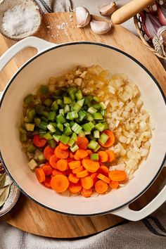 chopped vegetables are in a white bowl on a wooden cutting board next to garlic, carrots and onions