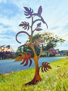 a metal tree sculpture sitting on top of a lush green field next to a lake