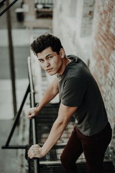 a young man leaning on the handrail of a set of stairs in front of a brick wall