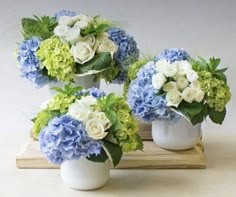 three white vases filled with blue and green flowers