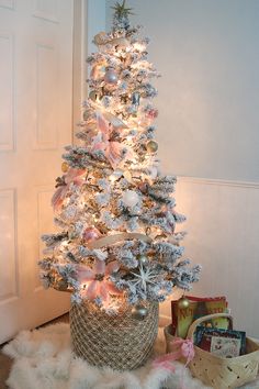 a white christmas tree with pink and silver ornaments in a basket on the floor next to presents