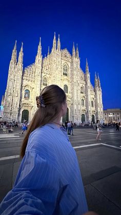 a woman standing in front of a large cathedral at night with her back to the camera