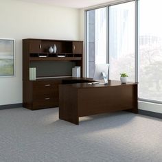 an empty office space with a desk and bookcase in front of a large window