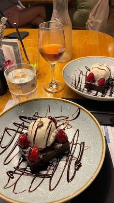 two plates with desserts on them sitting on a table next to glasses of wine