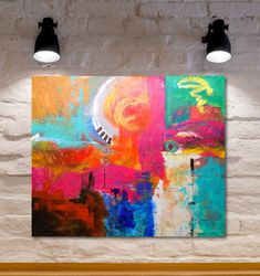 an abstract painting hangs on the wall next to two lamps and a brick wall behind it