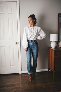 ashley wearing a white button up with balloon sleeves and a peter pan collar, straight leg full length mid-wash denim, cognac loafers and a gold pendant necklace standing next to a vintage wood dresser with a white table lamp Jean Outfits Dressy, Nice Outfits Dressy, Thanksgiving Outfit Women Casual, Thanksgiving Outfits Women, Stylish Capsule Wardrobe, Casual Thanksgiving Outfits, Outfit Ideas Dressy, Flare Jeans Outfit, Day Outfit Ideas