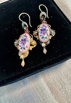 Victorian Earrings dangles tests for 10 & 14K gold, oval lovely enameled violets center with floral gold setting jeweled with genuine pearls and I believe a prong set Tourmaline.  Condition is very good for their age any slight wear commensurate with age, pictures show the details.  Length approx.- 1 7/8", wt for pair 4.8 grams.  True to the Victorian era love for nature-this aesthetic earring design is a splendid example.  Delicate and captivating. Elegant Pink Enamel Earrings, Vintage Enamel Wedding Earrings, Elegant Enamel Jewelry With Cabochon, Elegant Oval Enamel Jewelry, Vintage Pierced Enamel Earrings, Victorian Enamel Jewelry For Wedding, Victorian Enamel Wedding Jewelry, Vintage Enamel Jewelry With Matching Earrings, Oval Enamel Jewelry For Wedding