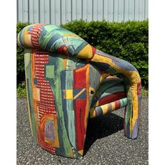 a colorful chair sitting on top of a gravel ground next to green bushes and shrubbery