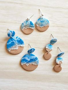 four different earrings with blue and white designs on them sitting on top of a wooden table