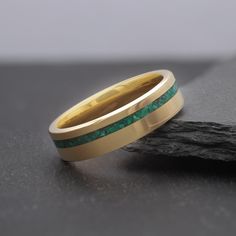 a wedding band with green and gold inlays on top of a piece of wood