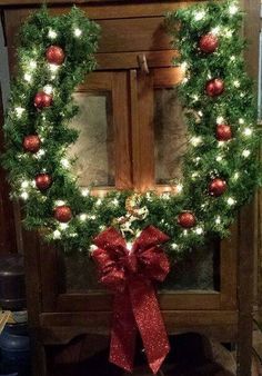 a christmas wreath with lights on it and a red bow hanging from the front door